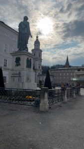 The bronze Wolfgang Amadeus Mozart statue standing tall in the historic square against a sunlit sky, viewed during a classic city tour salzburg.