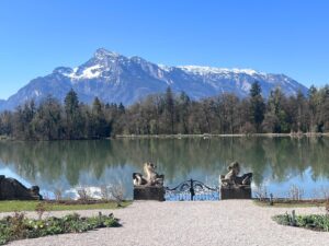 The snow-capped Untersberg mountain towers behind the serene waters and wrought-iron gates of the Leopoldskron lake during an Eco-conscious Sound of Music e-bike tour.