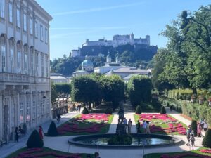 Beautiful pink flower beds and a grand fountain in Mirabell Gardens with the Hohensalzburg Fortress in the background, a key highlight of your Mirabell Gardens walking tour Salzburg.