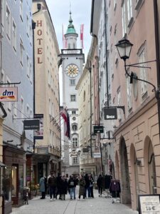 Travelers walking down the narrow cobblestone Getreidegasse shopping street toward the Rathaus clock tower during a relaxing salzburg walking tour.