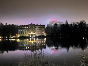 The illuminated facade of Schloss Leopoldskron reflects in the glassy water of the lake under a night sky, a spectacular sight detailed by a Private certified guide Sound of Music e-bike.