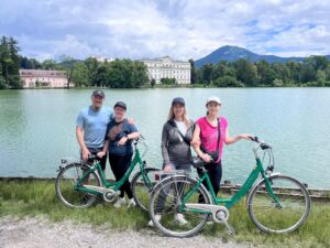 A family of four stands with their green bicycles by the serene Leopoldskroner Weiher lake during a premium Sound of Music E-Bike Tour in Salzburg, Austria.