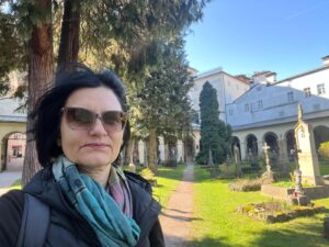 Expert local guide Annabelle Blanc standing on a path in the serene grassy courtyard of the Sebastiansfriedhof during a premium St Sebastian cemetery guided tour in Salzburg, Austria.